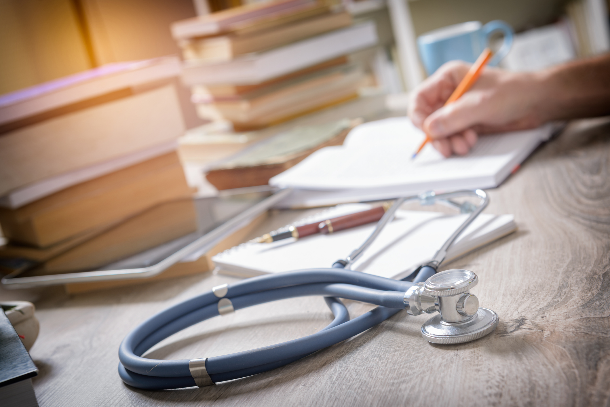 Medical journals with stethoscope and person writing in notebook